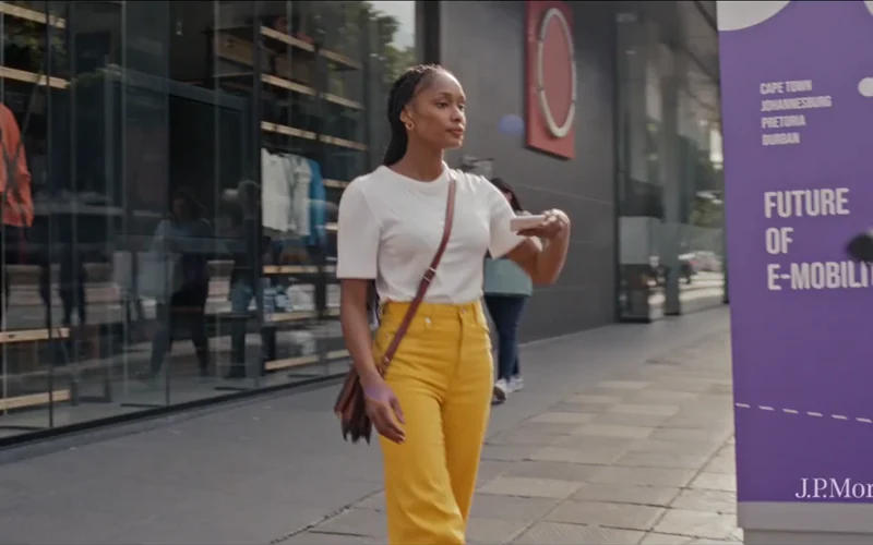 A woman in yellow trousers stands outside a city storefront in J.P. Morgan’s Anthem