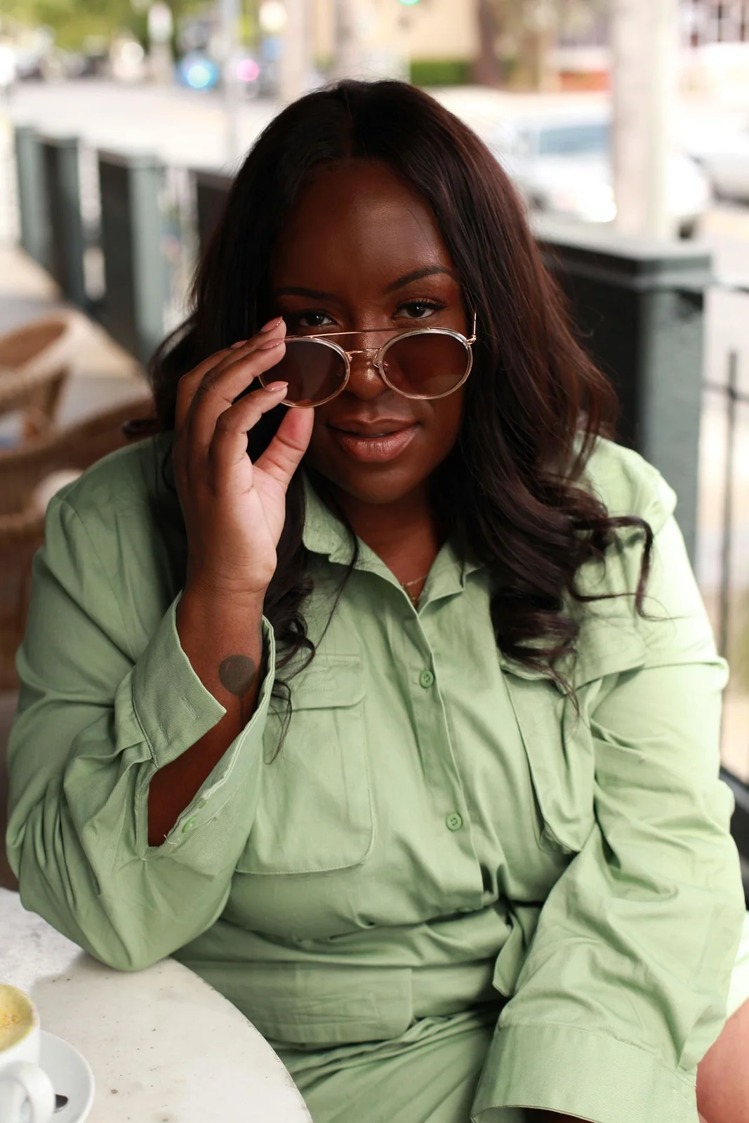Sophie Gold in a pale green outfit, lowering her sunglasses, in the original shots interview