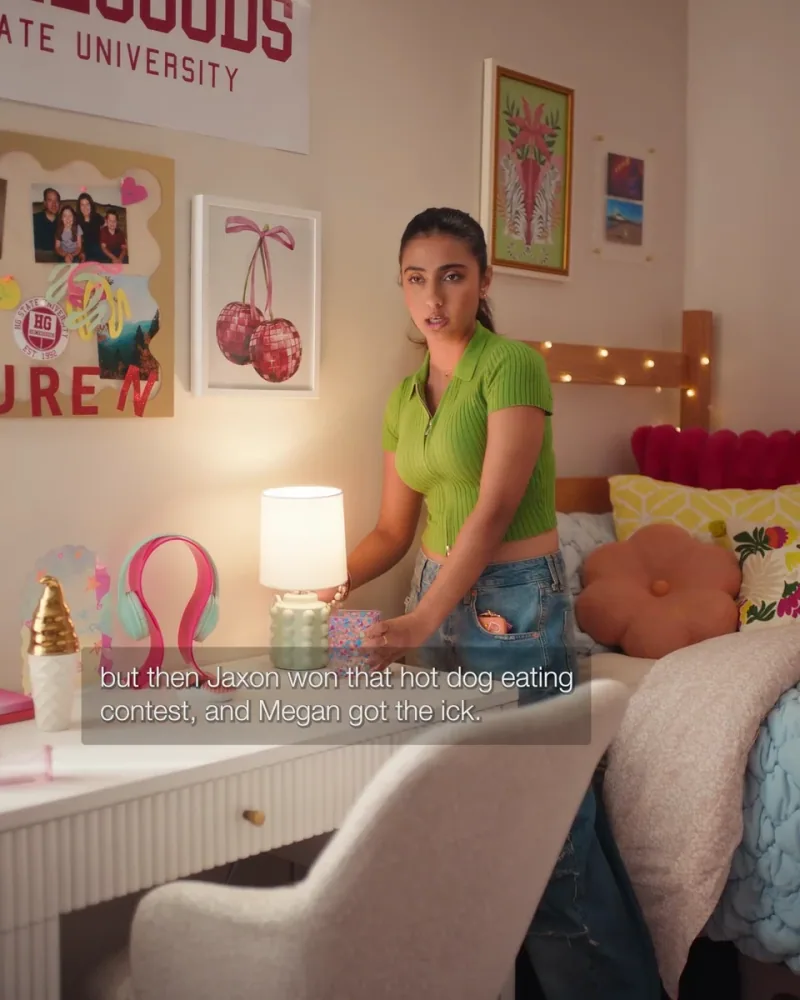 A student in a green shirt talks beside a desk and colourful dorm-room decorations in The Tea