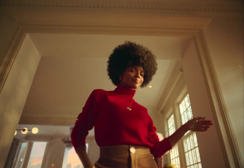 A woman in a red top dances in a sunlit interior.