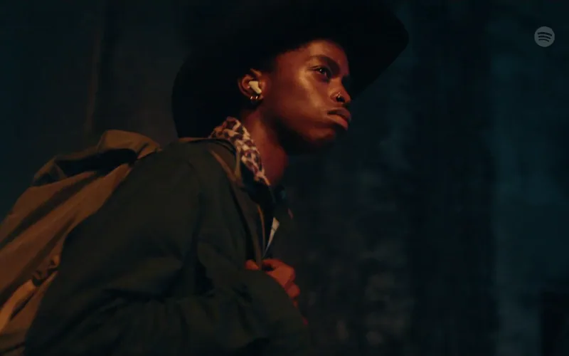 A young man wearing a black hat and earbuds turns toward the light.