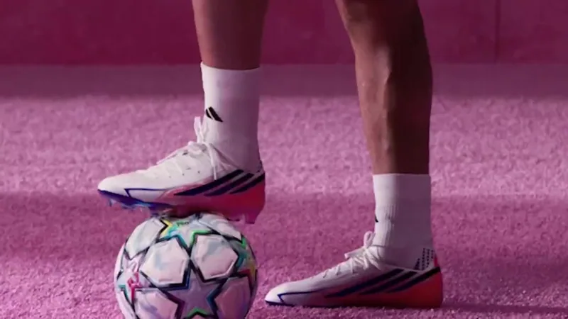 Football boots and a ball on a pink playing surface.