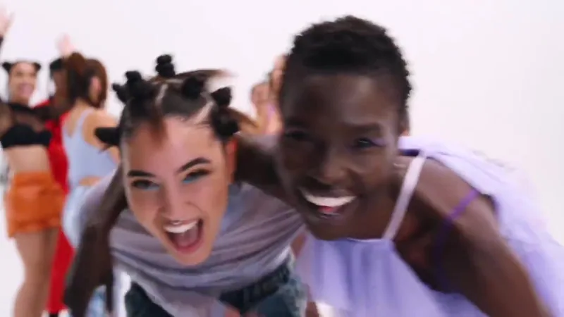 Two smiling performers lean towards the camera in a white studio.