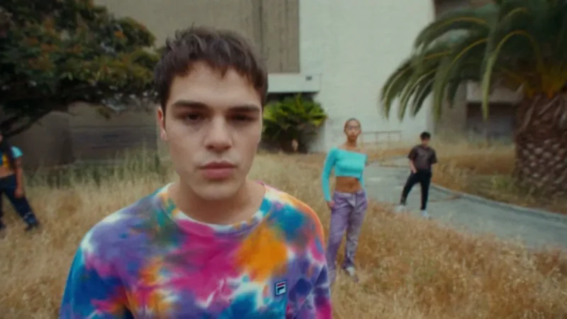 AJ Mitchell in a colourful shirt with dancers in a concrete courtyard.