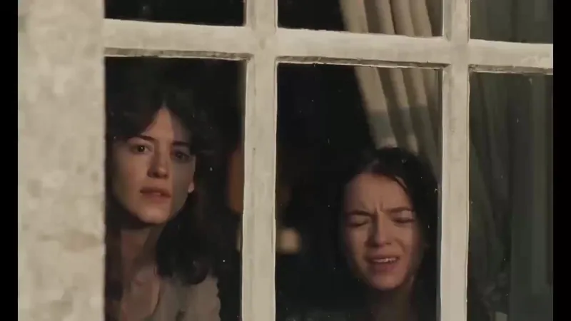 Two women in period clothing look through a window.