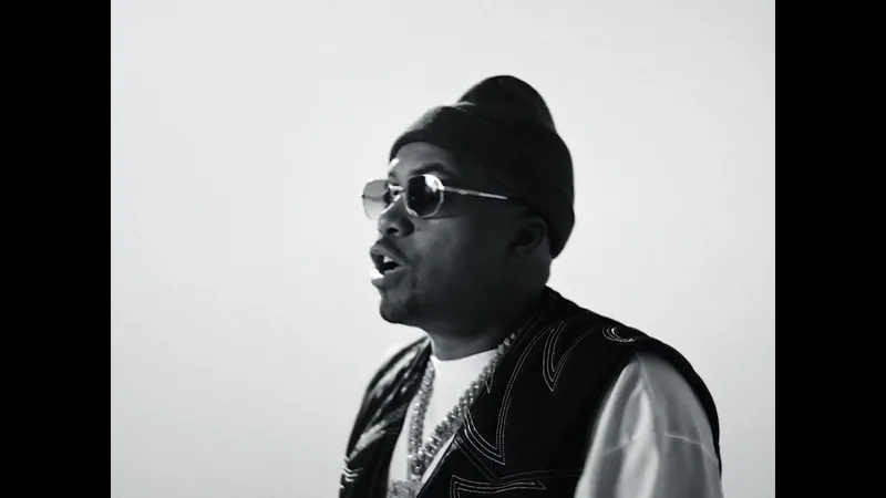 Nas wears sunglasses and a knit cap in a monochrome performance portrait.