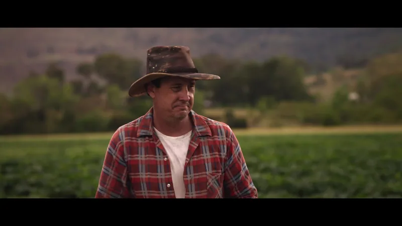 A farmer wearing a brown hat stands in a green field.