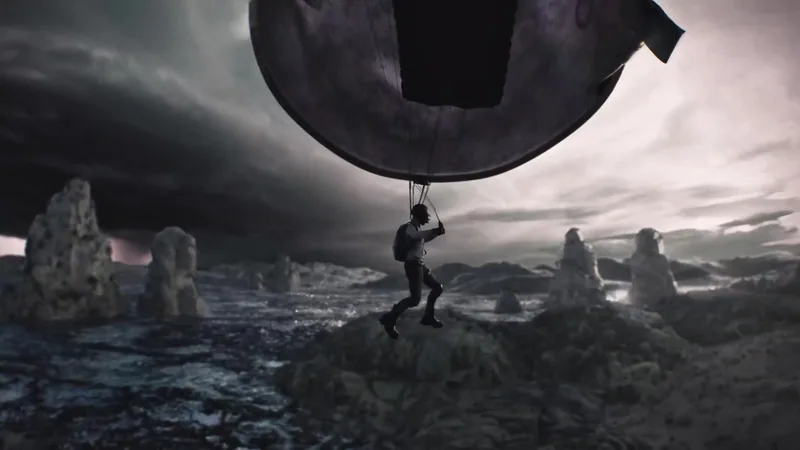 A figure hangs from a suspended car in a rocky landscape.