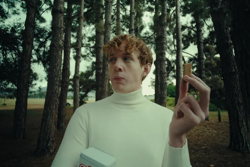 A red-haired man holds a biscuit in a forest.