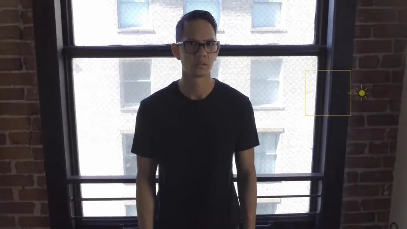 A man wearing glasses stands in front of a tall window.