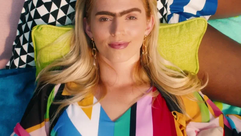 A woman in colourful clothing reclines against patterned summer cushions.