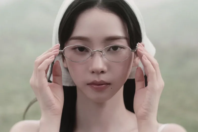 A woman holds glasses to her face against a misty landscape.
